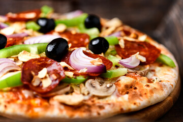 Pizza with chorizo ​​sausage, mozzarella cheese, green pepper and black olives. Rustic wooden background. Soft focus.	