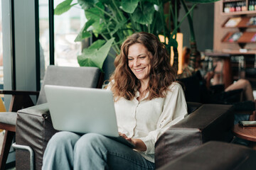 Beautiful happy cheerful woman working remotely online using a laptop while sitting in a cafe.