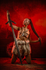 Viking woman warrior posing with long two handed sword on old wooden wall background in the red...