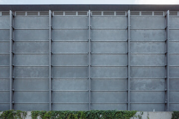 A straight-on photograph of a modern industrial building facade, creating a strong geometric background. The wall is constructed from a grid of gray metal or concrete panels set in a steel frame.