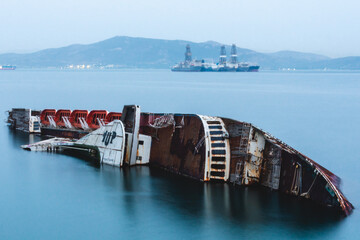 Rusty shipwreck in Elefsina bay with oil platforms, Attica, Greece.