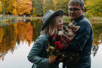 A man and woman stand by a serene lake, holding a dog