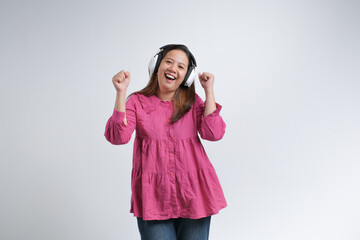 A cheerful young woman wearing a pink blouse and jeans enjoying music with wireless headphones,...