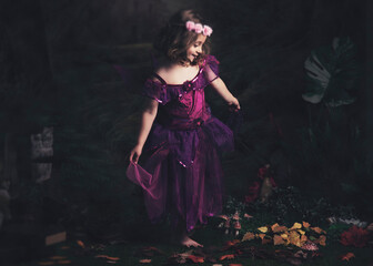 Fototapeta premium A young girl dressed as a fairy in a whimsical forest setting.