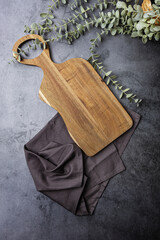 wooden cutting board on dark background with cloth and plant