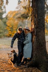 A young Caucasian couple stands by a tree in an autumn park. The woman wears a hat and a coat. Two...
