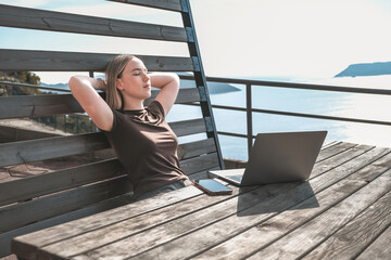 Digital nomad working remotely on laptop at seaside terrace; coastal town and islands behind....