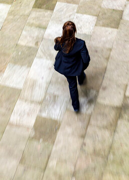 A woman in a suit walks on a stone path.