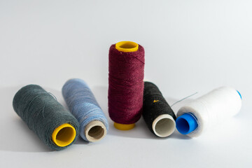 A scattered group of five spools of thread in various colors, isolated on a clean white background,...