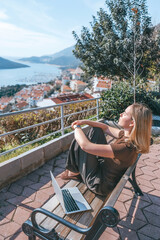 Digital nomad working remotely on laptop at seaside terrace; coastal town and islands behind....