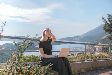Digital nomad working remotely on laptop at seaside terrace; coastal town and islands behind....