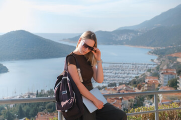 Digital nomad working remotely on laptop at seaside terrace; coastal town and islands behind....