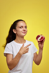 Beautiful happy woman holding pomegranate on yellow background