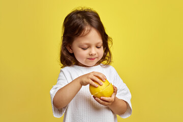 cute funny little child girl holding lemon on yellow background