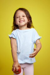 cute Caucasian little child girl holding apple on yellow background, Healthy nutrition