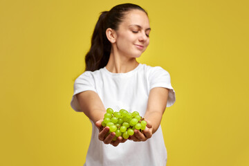 portrait of attractive Caucasian smiling woman holds grapes isolated on yellow studio background,...