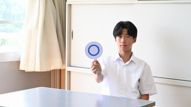 学校の教室でクイズに答える男子学生　○&times;で回答する学習シーン