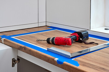 red cordless electric drill screwdriver and measuring tape on kitchen countertop. Kitchen cabinet installation