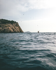 Surreal Scene of a Man Holding a Spoon in the Sea with Majestic Mountain Landscape