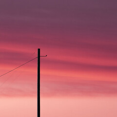 A solitary pole stands silhouetted against a vibrant, pink and purple gradient sky at dusk. Minimalist and striking, evoking themes of connection, isolation, and the beauty of twilight.