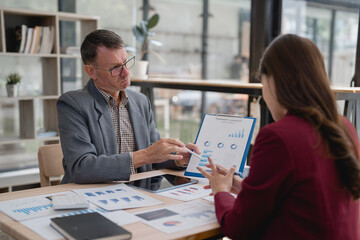 Senior manager explaining marketing strategy showing charts to young businesswoman during office meeting analyzing financial graphs using pen and digital tablet while working together at desk