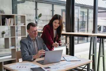 Two business colleagues reviewing marketing data displayed on laptop and digital tablet, working together in modern office environment, analyzing graphs and charts, collaborating on project