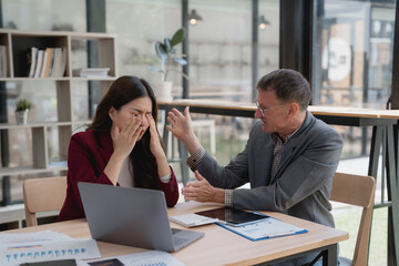 Business partners arguing during a meeting, with a businesswoman rubbing her eyes and a manager scolding an employee amid stress and frustration in a modern office