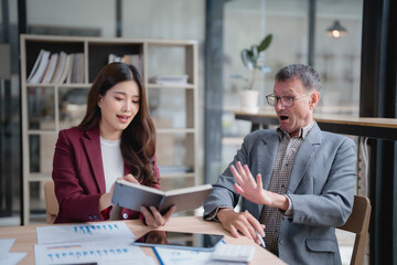 Asian businesswoman presenting unexpected financial results to a senior businessman, capturing his surprised expression during a crucial meeting in the office environment