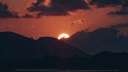 The sun sets behind a dark mountain with glowing red and orange tones in the sky.