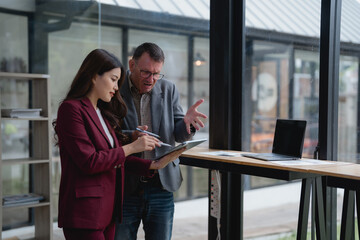 Two business professionals engaged in a project discussion, utilizing a tablet in a sleek, modern office. Collaborating effectively, they share innovative ideas for driving company success