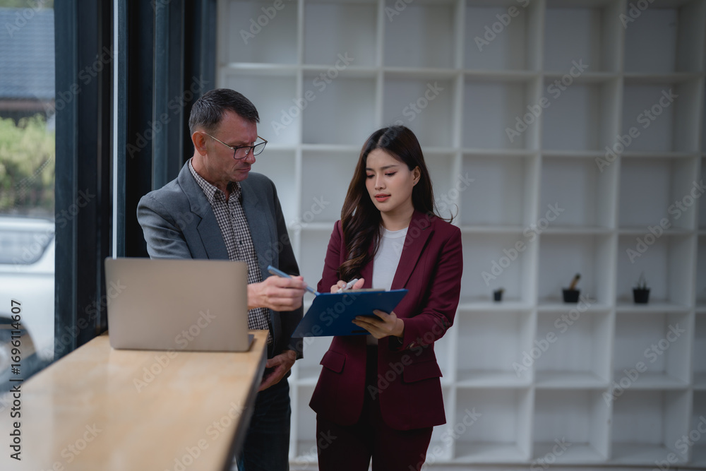 Poster Two businesspeople in suits engaging in a focused discussion, utilizing a laptop and clipboard to review notes and strategize for upcoming projects and tasks