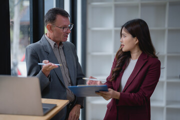 Businesspeople discussing and brainstorming in a modern office, with a senior businessman explaining ideas to a young businesswoman while collaborating on a project