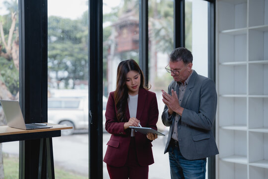 Businesswoman displaying information on a digital tablet while engaging in a work discussion with a businessman in a modern office setting, fostering collaboration and strategic planning