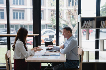 Business partners reviewing financial charts and graphs while discussing company performance and growth strategies at an office desk, collaborating on investment planning