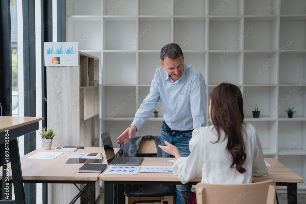 Poster smiling manager engaging in a discussion with an employee while pointing at charts and graphs laid o