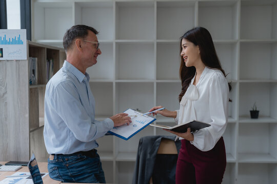Two business colleagues discussing marketing strategy while analyzing financial statistics on paperwork in a professional office environment
