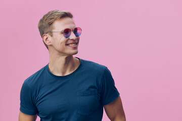 Smiling young man wearing sunglasses blue t-shirt standing look aside isolated on pink background...