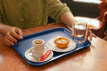 Close up middle age woman tries Portuguese egg tart pastry called Pastel de Nata with coffee near bakery in Lisbon. Solo tourism and travel. Part of a series