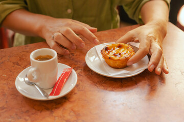 Close up middle age woman tries Portuguese egg tart pastry called Pastel de Nata with coffee near bakery in Lisbon. Solo tourism and travel. Part of a series