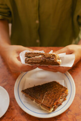 Gen Z middle age woman tries traditional Portuguese fast food toast with bacon and cheese in Lisbon. Solo tourism and travel. Part of a series
