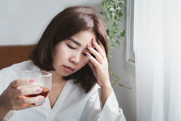 stressed Asian woman holding a whiskey glass, suffering from headache and feeling drunk....