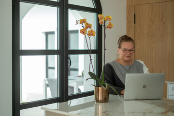 Middle-aged woman working on laptop in modern office environment, surrounded by natural light and...