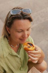 Gen Z middle age woman tries Portuguese egg tart pastry called Pastel de Nata near bakery in Lisbon. Solo tourism and travel.