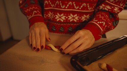 Person in Festive Sweater Placing Twisted Dough on Baking Sheet Lined with Parchment Paper, Close View, Candy Cane Cookie Crafting Concept
