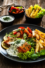 Fried salmon steak with tzatziki sauce, homemade potato fries and tomato salad on wooden table
