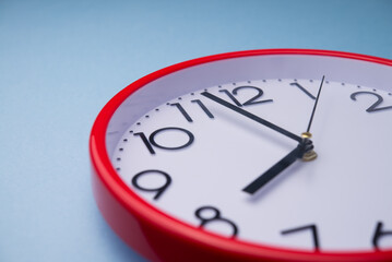 Close up clock hands of white red analog round wall clock face with blue background. Abstract deadline, last minute, in time, on time, time management and so on concept.