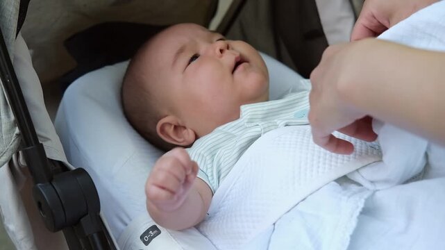 Little asian baby boy is lying outdoor in a stroller
