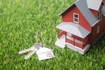 Red house model and house key on green grass background copy space. Homebuyers, mortgage loan, banking, real estate investment trust (REIT), reverse mortgage, home selling or rental concept.