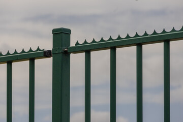 Green metal security fence with spikes protecting property under cloudy sky