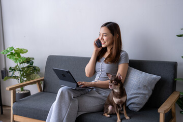 A woman is sitting on a couch talking on her cell phone while her dog is laying